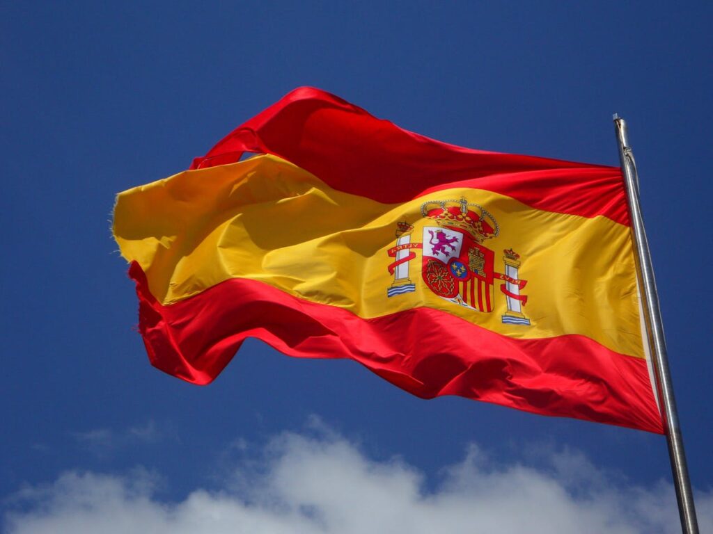 Vibrant Spanish flag waving against a clear blue sky and clouds.